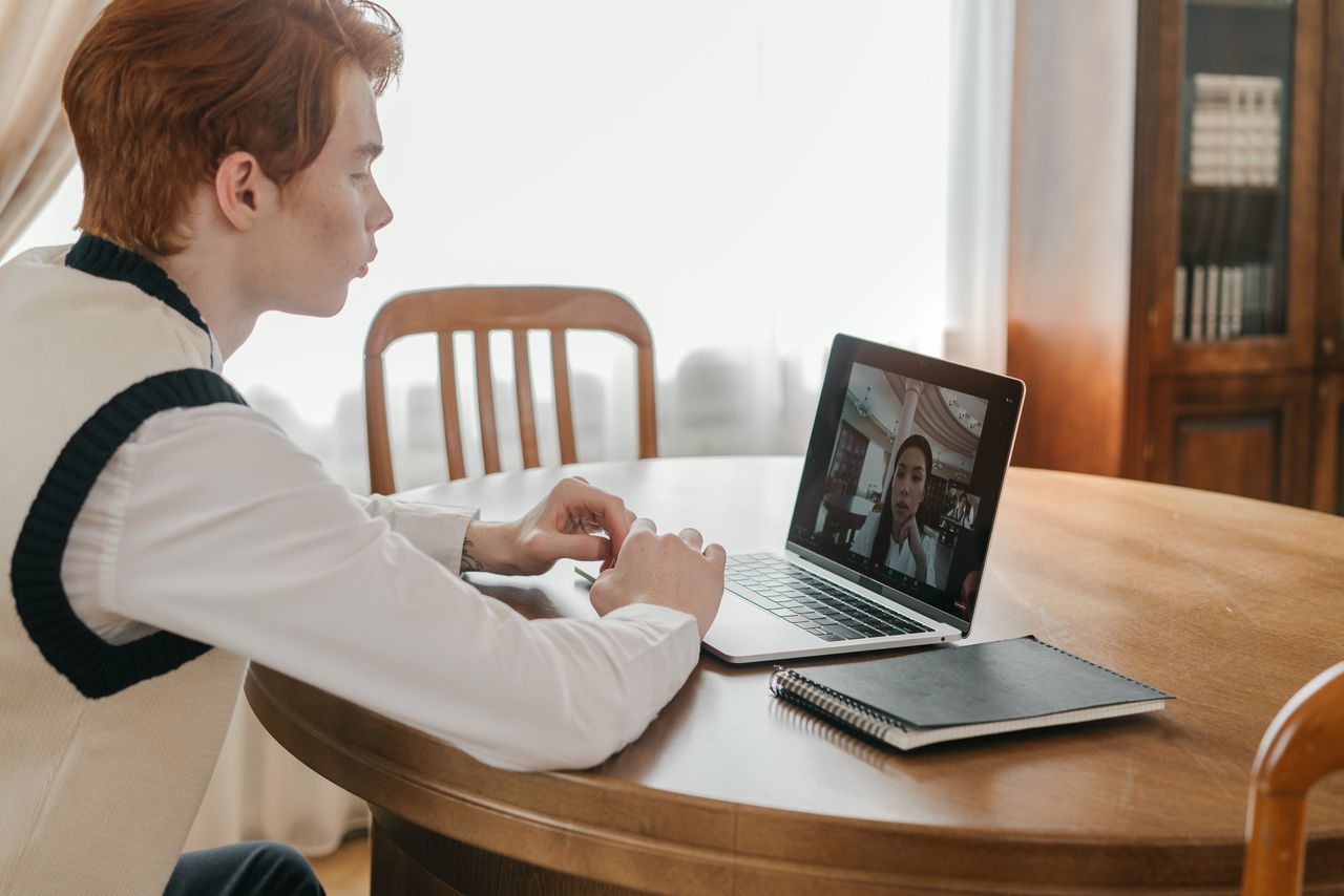 Jeune homme participant à un appel vidéo sur un ordinateur portable à la maison, illustrant une communication à distance.